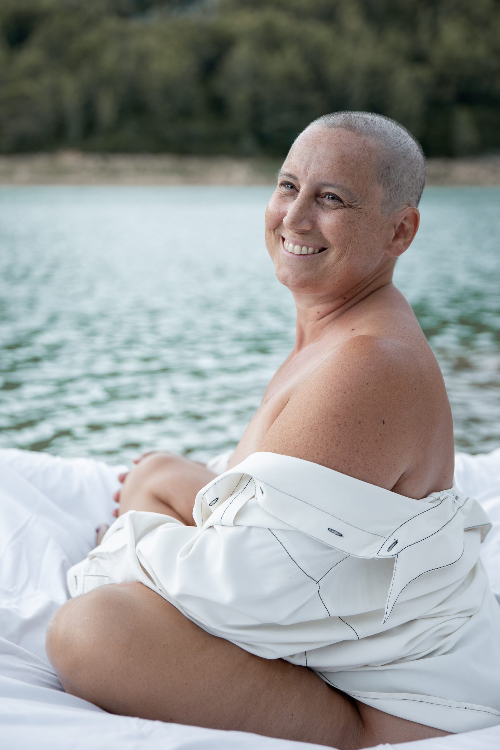 femme rasée par le cancer souriante sur le bord d'un lac